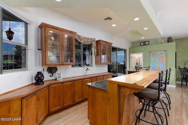 kitchen featuring brown cabinetry, visible vents, light wood-style floors, and a kitchen breakfast bar