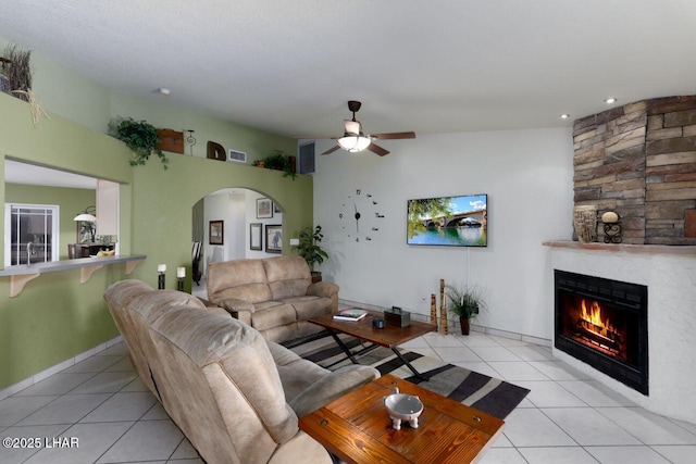 living room with light tile patterned floors, arched walkways, a large fireplace, and a ceiling fan