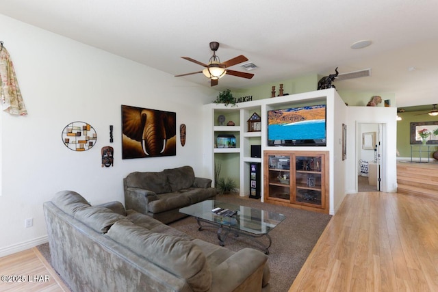 living room featuring baseboards, visible vents, a ceiling fan, and wood finished floors