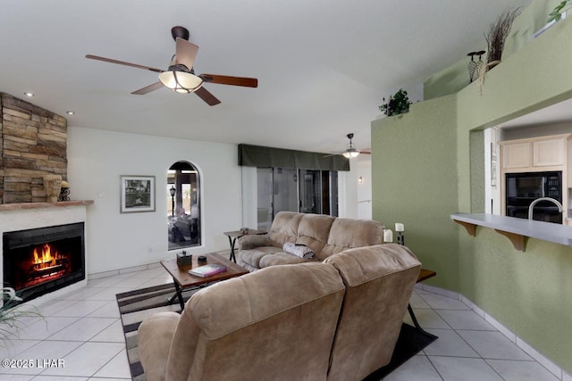 living area featuring a large fireplace, ceiling fan, light tile patterned floors, and baseboards