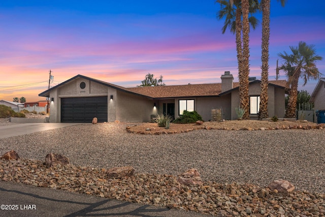 view of front of home featuring driveway, a garage, a chimney, and stucco siding