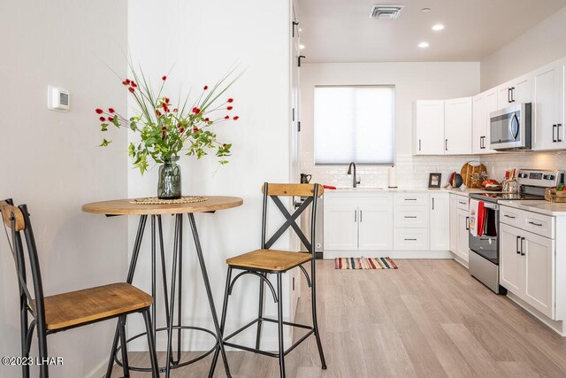 kitchen with stainless steel appliances, white cabinetry, tasteful backsplash, and light hardwood / wood-style floors