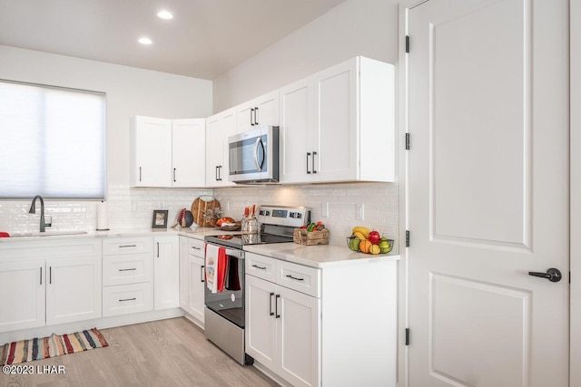 kitchen with sink, white cabinetry, light hardwood / wood-style flooring, appliances with stainless steel finishes, and decorative backsplash