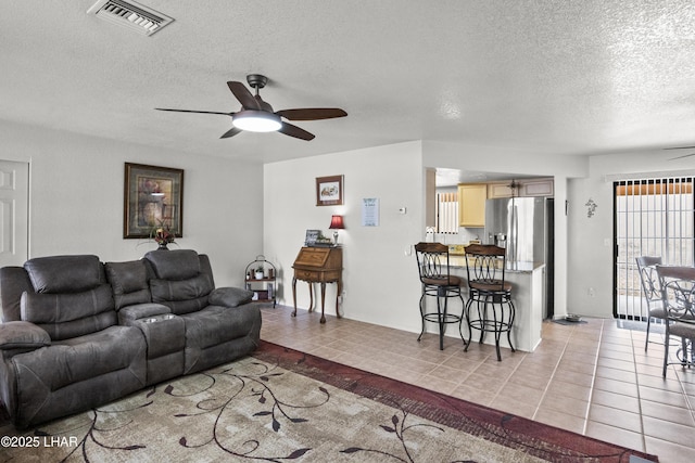 living room with a textured ceiling, light tile patterned floors, ceiling fan, and visible vents