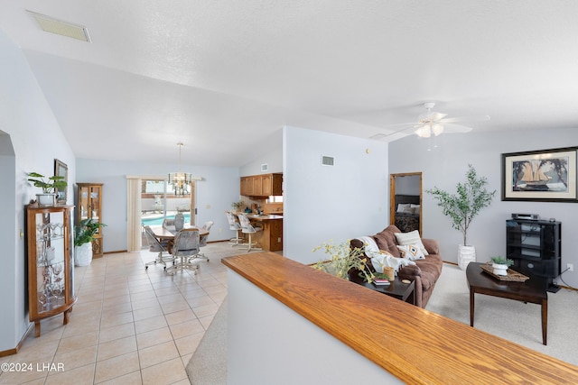 living room featuring ceiling fan with notable chandelier, lofted ceiling, visible vents, and light tile patterned floors