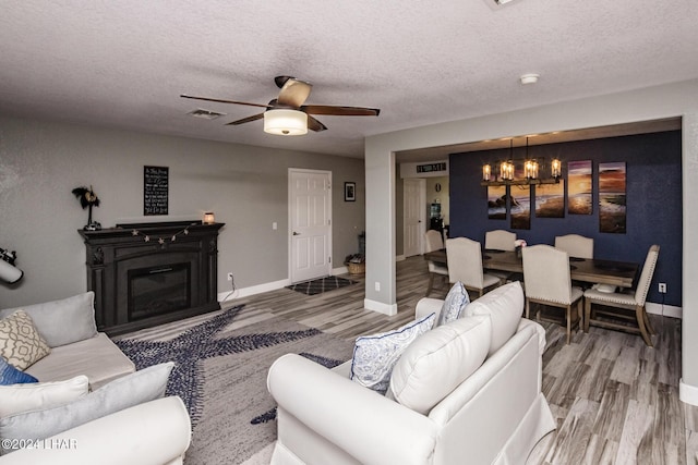 living room with wood-type flooring, ceiling fan with notable chandelier, and a textured ceiling