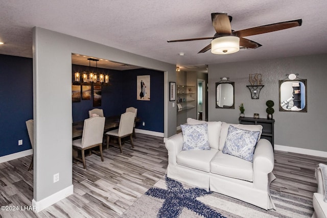 living room featuring ceiling fan with notable chandelier, wood-type flooring, and a textured ceiling