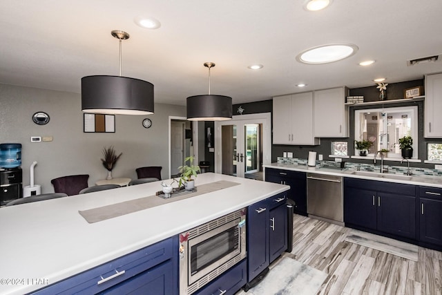 kitchen with blue cabinetry, sink, white cabinetry, appliances with stainless steel finishes, and pendant lighting