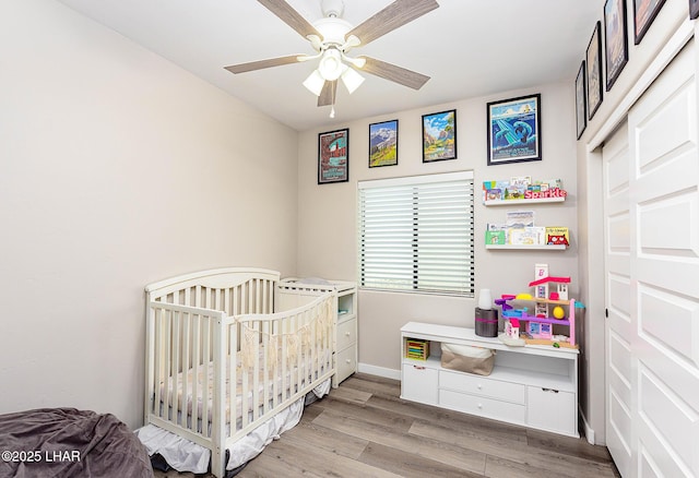 bedroom featuring light wood-style flooring, ceiling fan, a crib, and baseboards