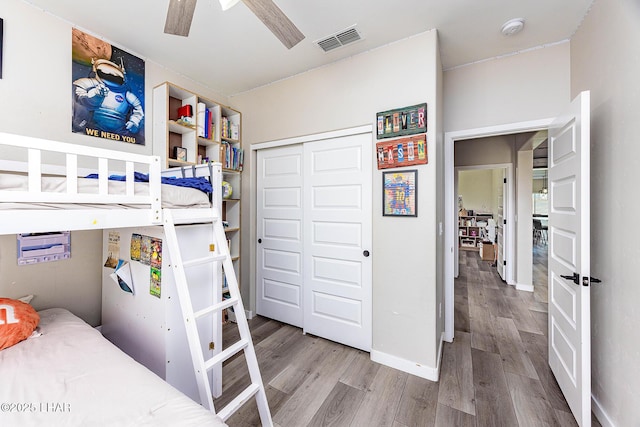 bedroom featuring wood finished floors, a ceiling fan, visible vents, baseboards, and a closet