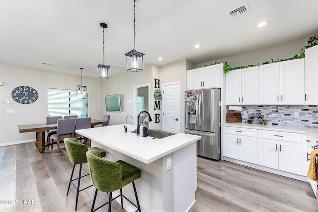 kitchen with a sink, visible vents, stainless steel refrigerator with ice dispenser, light wood finished floors, and tasteful backsplash