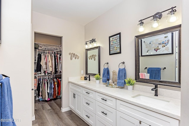 bathroom with double vanity, wood finished floors, a sink, and a walk in closet