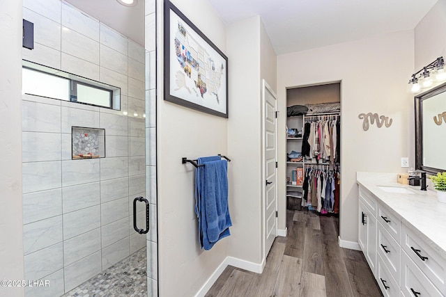 bathroom with a walk in closet, a stall shower, vanity, wood finished floors, and baseboards