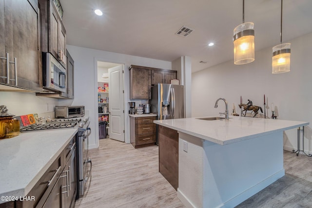 kitchen featuring light stone counters, decorative light fixtures, stainless steel appliances, and an island with sink