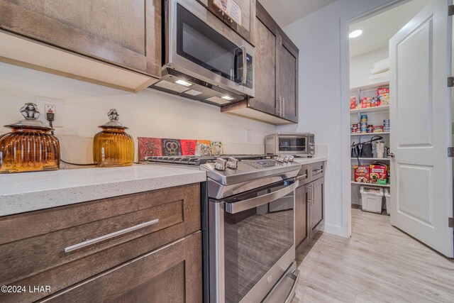 kitchen with light stone counters, dark brown cabinetry, light hardwood / wood-style floors, and appliances with stainless steel finishes