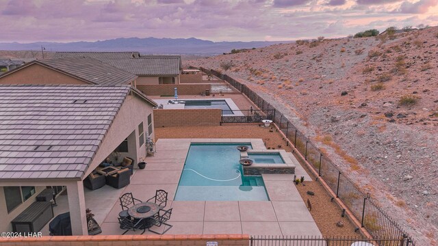 pool at dusk featuring an in ground hot tub, a mountain view, and a patio area