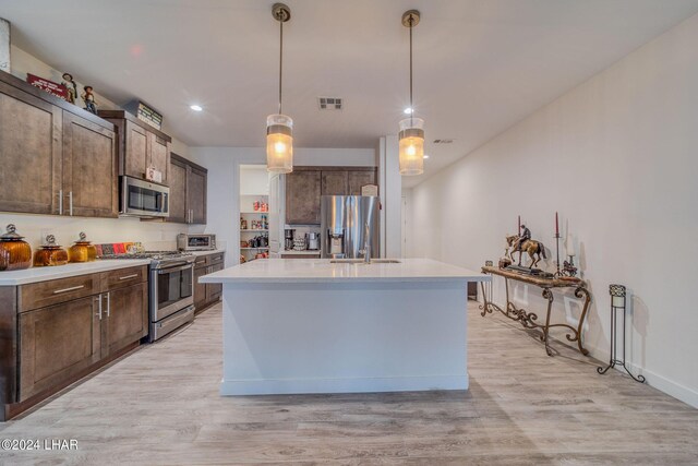 kitchen featuring light hardwood / wood-style flooring, appliances with stainless steel finishes, hanging light fixtures, dark brown cabinetry, and an island with sink