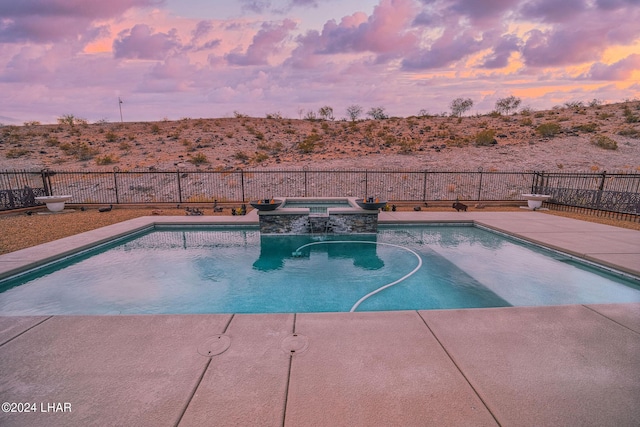 pool at dusk with an in ground hot tub and a patio area