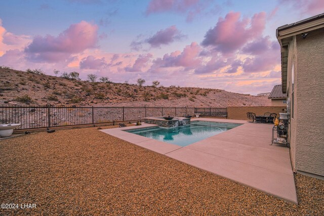 pool at dusk featuring a patio and an in ground hot tub