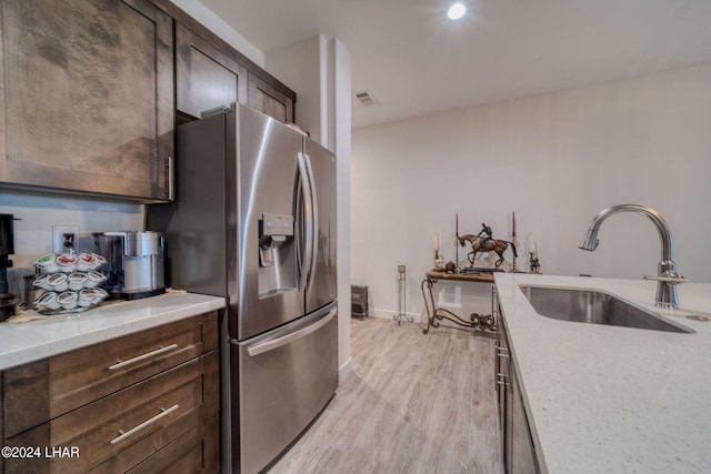 kitchen with stainless steel fridge with ice dispenser, sink, dark brown cabinetry, light stone counters, and light wood-type flooring