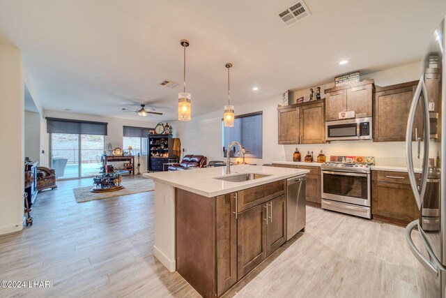 kitchen featuring sink, stainless steel appliances, light hardwood / wood-style floors, an island with sink, and decorative light fixtures