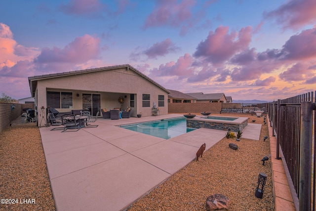 pool at dusk featuring an in ground hot tub and a patio area