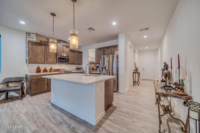 kitchen featuring appliances with stainless steel finishes, sink, hanging light fixtures, light hardwood / wood-style floors, and a center island with sink