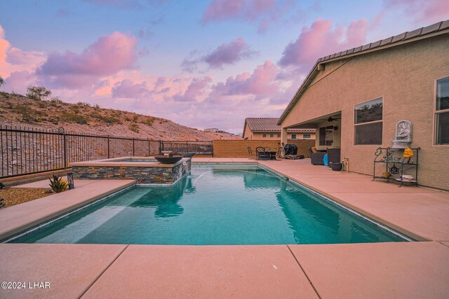 pool at dusk featuring a mountain view, a patio, and an in ground hot tub