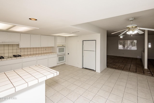 kitchen featuring tasteful backsplash, tile counters, light tile patterned flooring, white cabinets, and white appliances