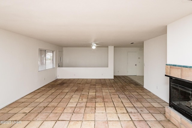 empty room featuring a tiled fireplace and ceiling fan