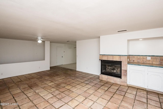 unfurnished living room with a fireplace, visible vents, and ceiling fan