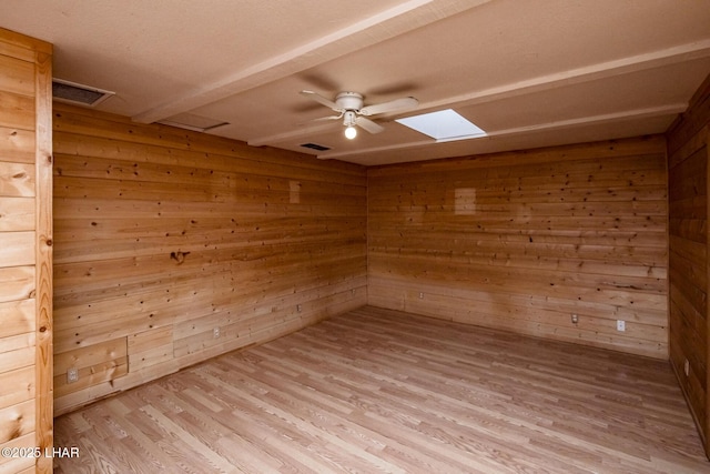 empty room with light wood finished floors, wooden walls, visible vents, attic access, and a skylight