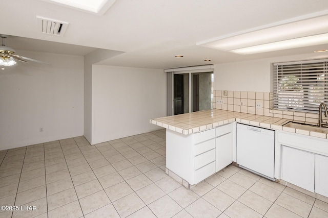 kitchen featuring visible vents, a sink, a peninsula, dishwasher, and tile counters