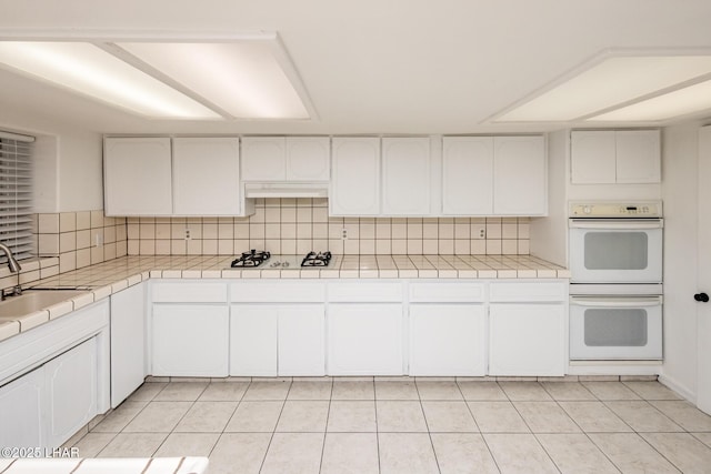 kitchen with backsplash, tile counters, light tile patterned floors, white appliances, and a sink