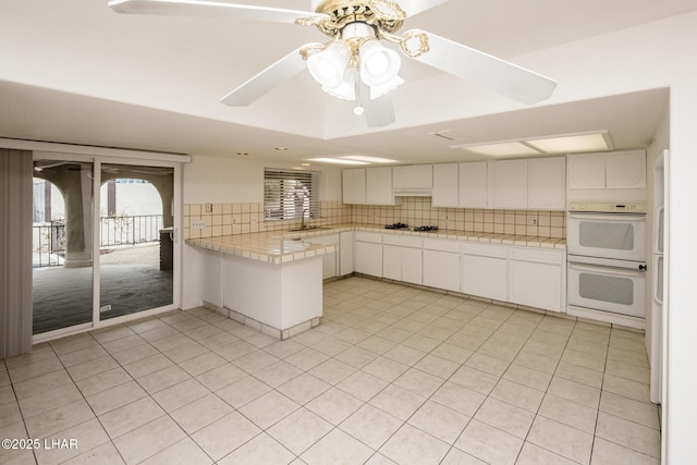 kitchen featuring backsplash, stovetop, double oven, a peninsula, and white cabinets