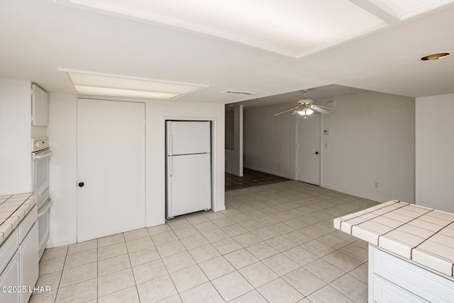 kitchen with white appliances, a ceiling fan, visible vents, tile counters, and white cabinetry