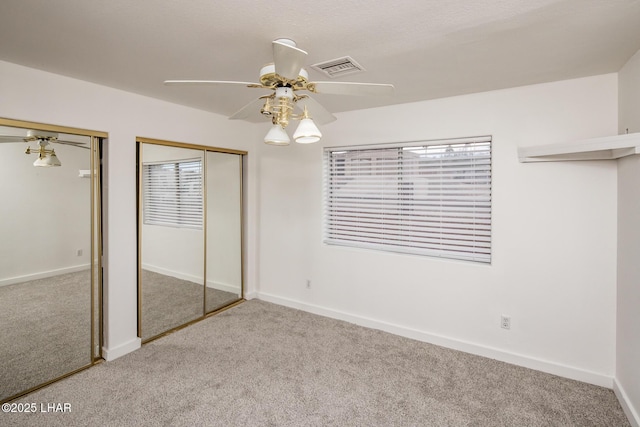 unfurnished bedroom featuring carpet flooring, visible vents, multiple closets, and baseboards