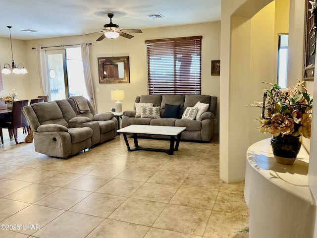 living area featuring visible vents, light tile patterned flooring, and ceiling fan with notable chandelier