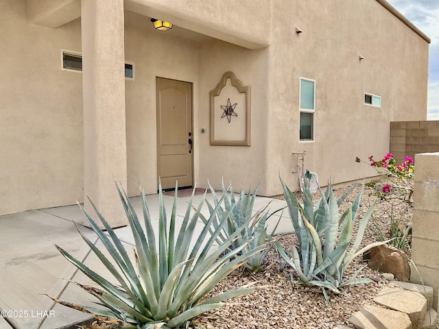 view of exterior entry with stucco siding and fence