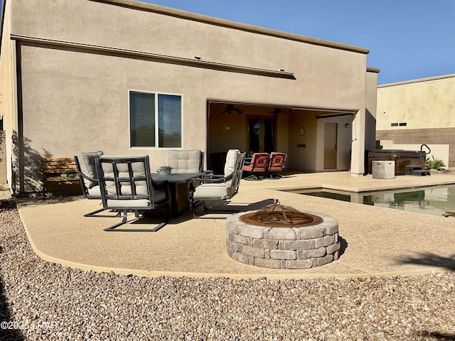 back of property with fence, stucco siding, a hot tub, a fire pit, and a patio area