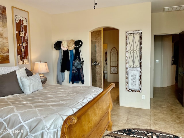 tiled bedroom featuring visible vents, arched walkways, and ensuite bath