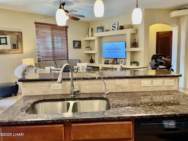 kitchen with dishwasher, dark stone countertops, open floor plan, and a sink