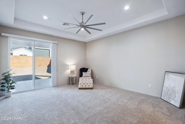 sitting room featuring a raised ceiling, carpet, and ceiling fan