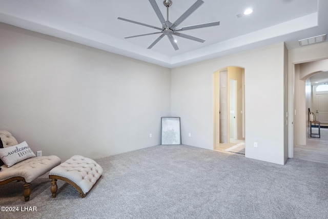 living area with light carpet, a tray ceiling, and ceiling fan