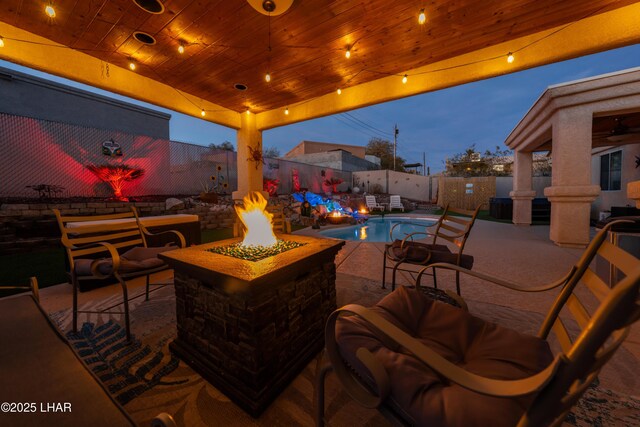 patio terrace at dusk with a fenced in pool and a fire pit