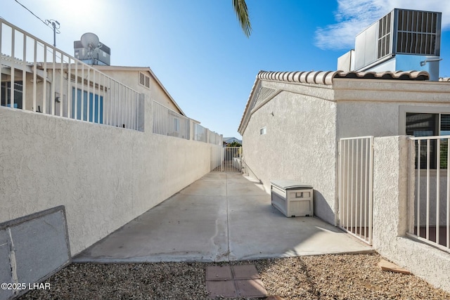 view of side of property with a tiled roof, stucco siding, a patio area, and fence