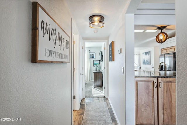 corridor featuring baseboards, a textured ceiling, wood finished floors, and a textured wall