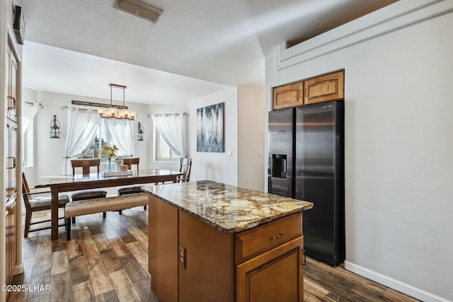 kitchen with visible vents, dark wood-type flooring, stainless steel fridge with ice dispenser, light stone counters, and brown cabinets