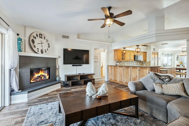 living room with visible vents, light wood finished floors, lofted ceiling, ceiling fan, and a tiled fireplace