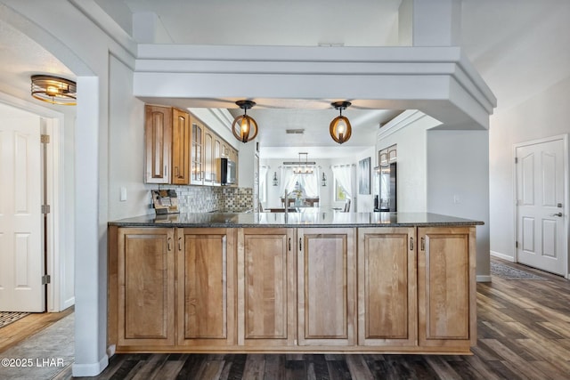 kitchen with dark stone countertops, brown cabinetry, dark wood finished floors, a peninsula, and decorative backsplash